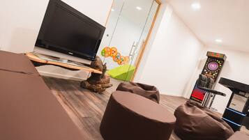 A modern living room with a flat-screen TV, bean bag chairs, a treadmill, and a wall with colorful artwork.