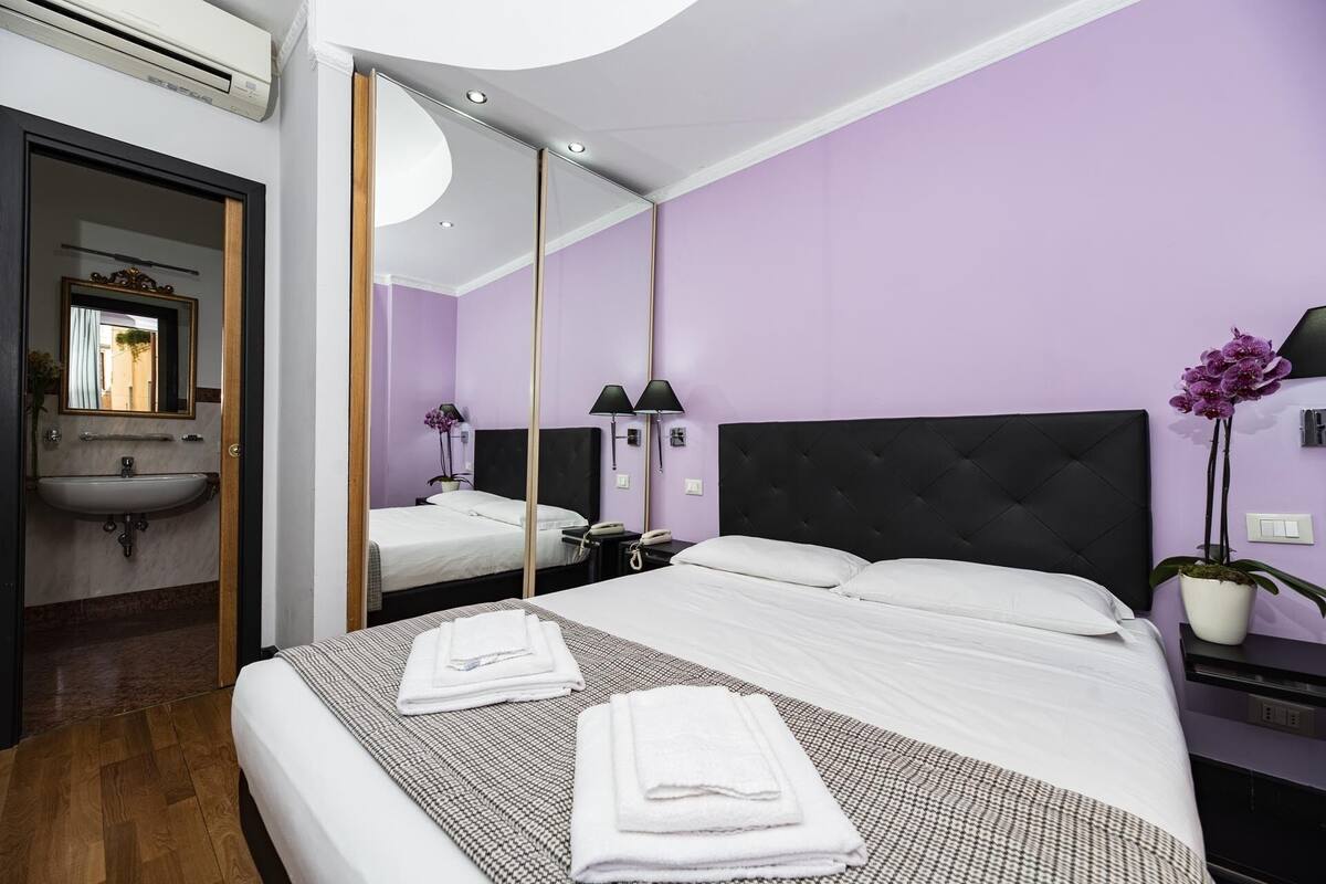 Une chambre d’hôtel comprenant un lit, des lampes de chevet, une table de chevet, un miroir, un lavabo et un pot d’orchidée.