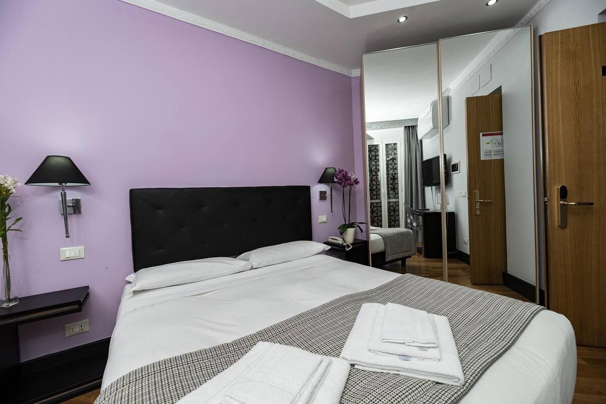Une chambre d’hôtel avec un grand lit, une table de chevet avec une lampe, un miroir et une armoire.