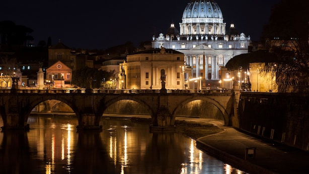 A nighttime view of a historic bridge with a large domed building in the background.