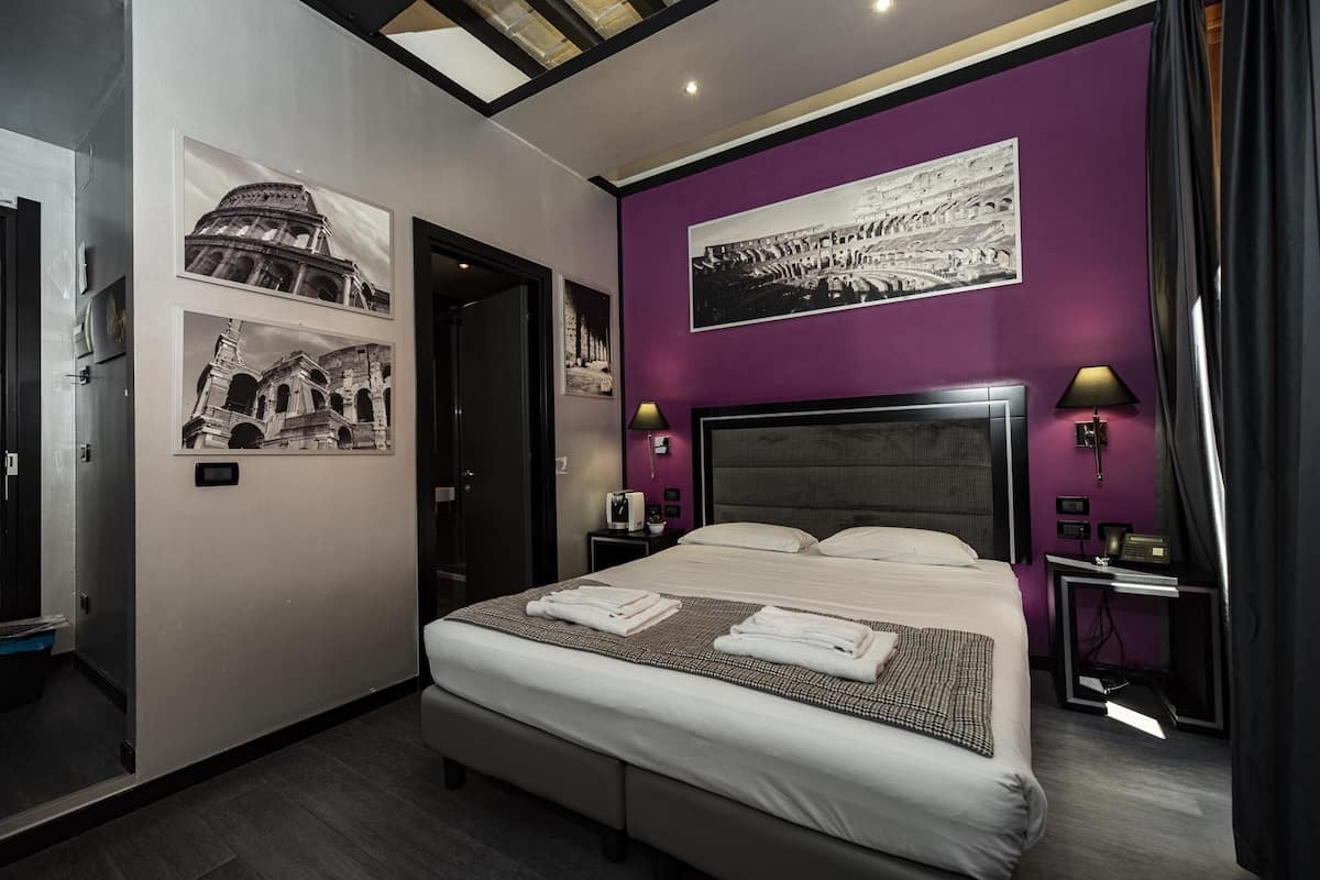 Une chambre d’hôtel moderne avec un grand lit, deux tables de chevet, une tête de lit et un luminaire au plafond.
