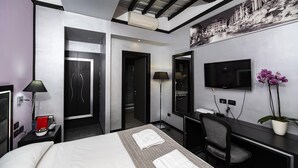 A modern hotel room with a bed, desk, chair, and a flat-screen TV.