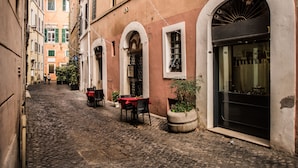 A cobblestone street with a café featuring outdoor seating, stone planters, and a black-framed window.