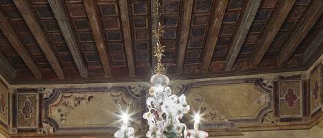 Habitación de hotel clásica con una cama grande, un banco tapizado en rojo, dos mesitas de noche con lámparas y un candelabro.