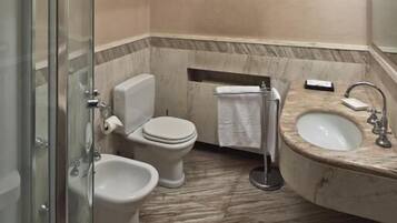 A bathroom with a glass-enclosed shower, a toilet, a bidet, and a sink.