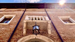 A brick building with a large arched entrance, two windows, and a hanging lantern. - Albergo Cappello (Ravenna)