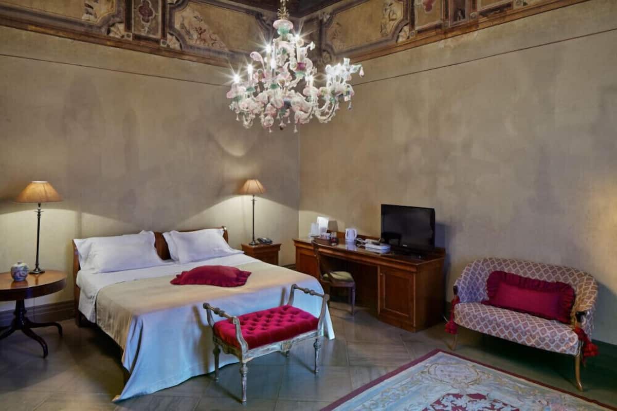 A bedroom with a large bed, a desk with a computer, a TV, a chair, and a sofa.