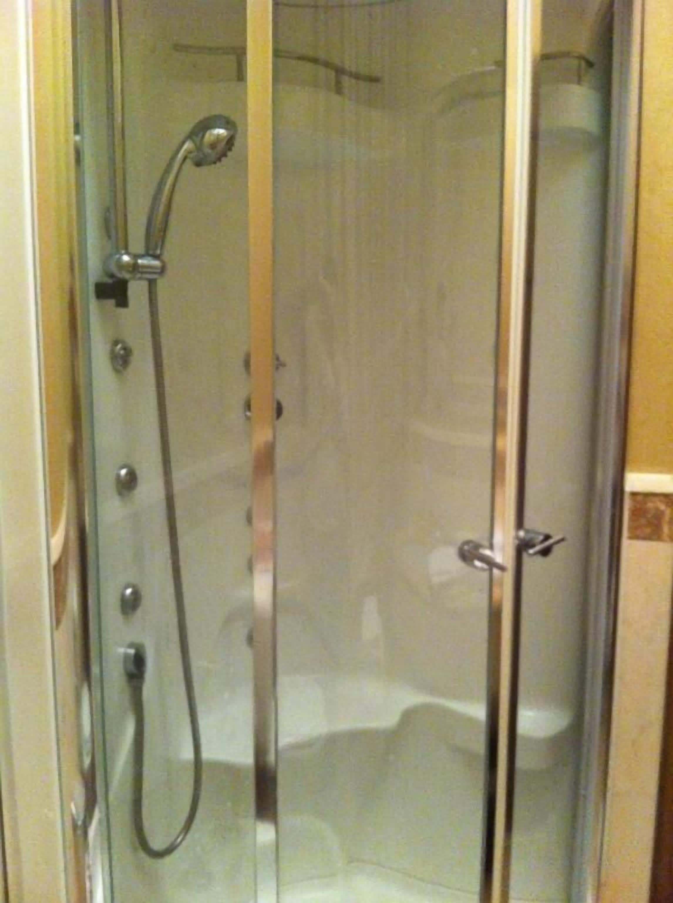 A glass-enclosed shower stall with a handheld showerhead and a control panel.