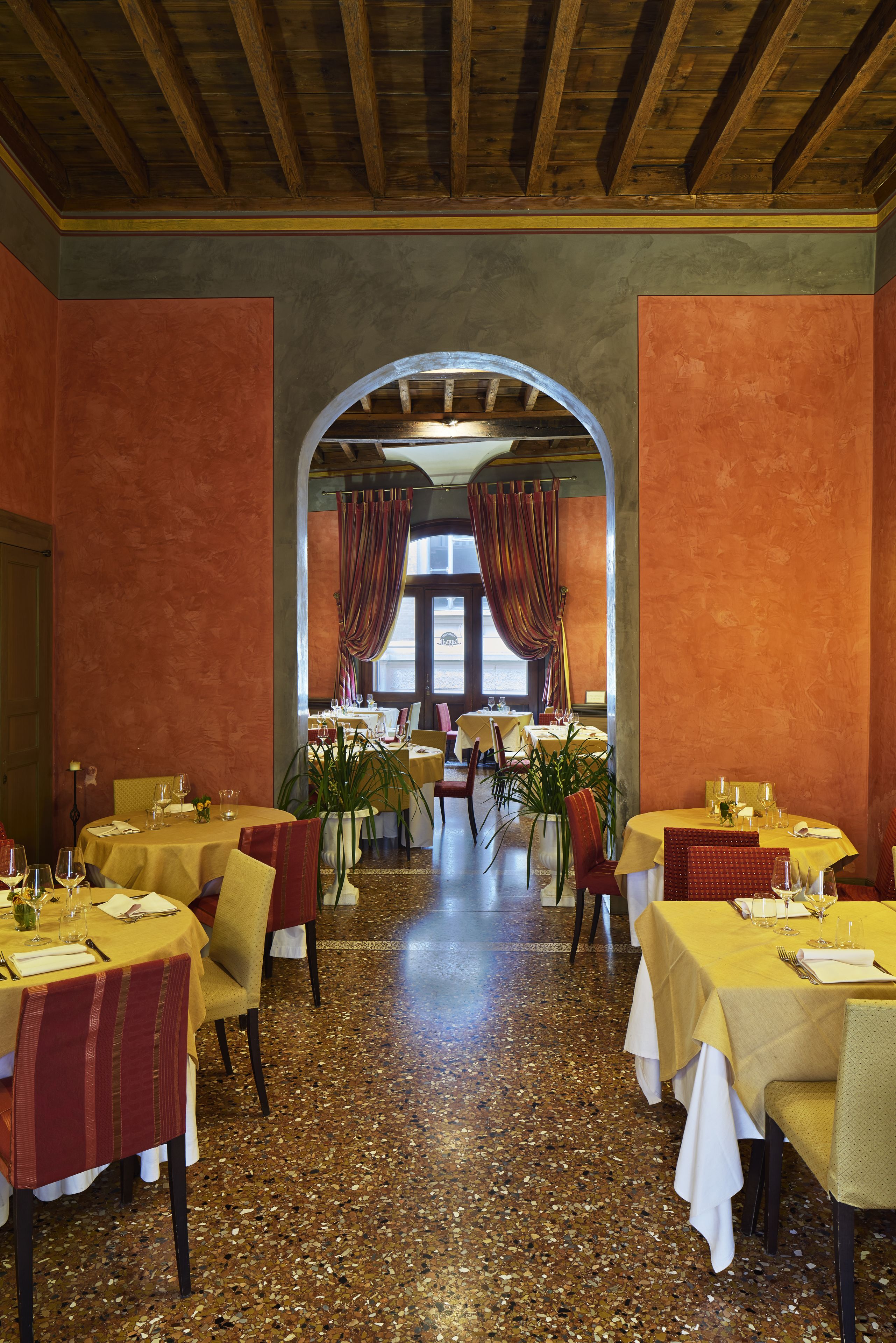 Un restaurant avec des tables dressées, un plafond en bois et une vue sur l’extérieur, accessible par une arche.