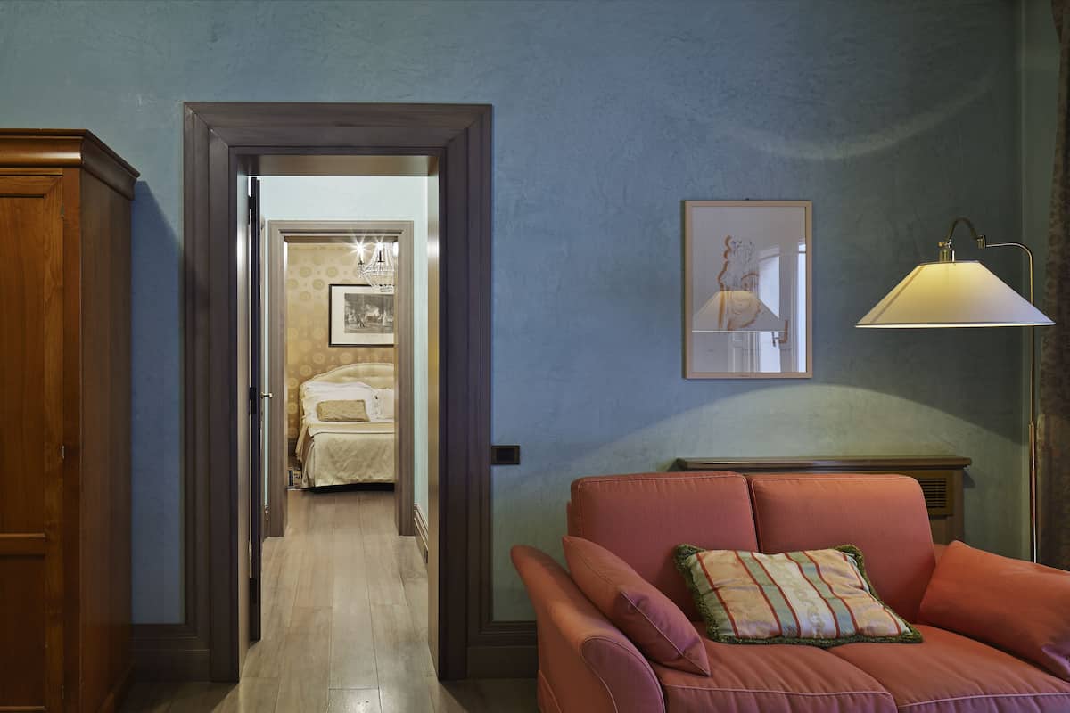 A room with a wooden door, a red sofa with a patterned pillow, a framed picture on the wall, and a lamp.