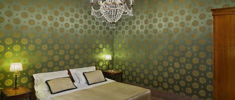 A hotel room with a large bed, two bedside tables, a chandelier, and patterned wallpaper.