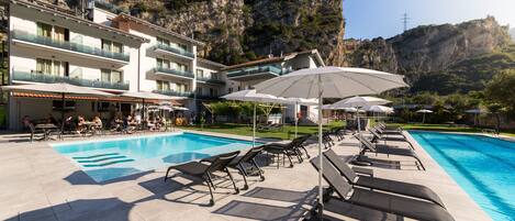 A hotel pool area with sun loungers and umbrellas, surrounded by a mountainous landscape.