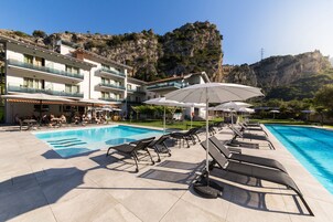 Zona de piscina de hotel con tumbonas y sombrillas, rodeada de un paisaje montañoso.