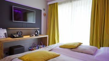 Une chambre d’hôtel avec un lit, un téléviseur fixé au mur, un bureau avec une machine à café et des rideaux jaunes.