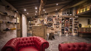 A room with a stone floor, wooden ceiling, and red leather chairs. There are shelves with wine bottles and a bar area. - Aktivhotel Santalucia (Nago-Torbole)