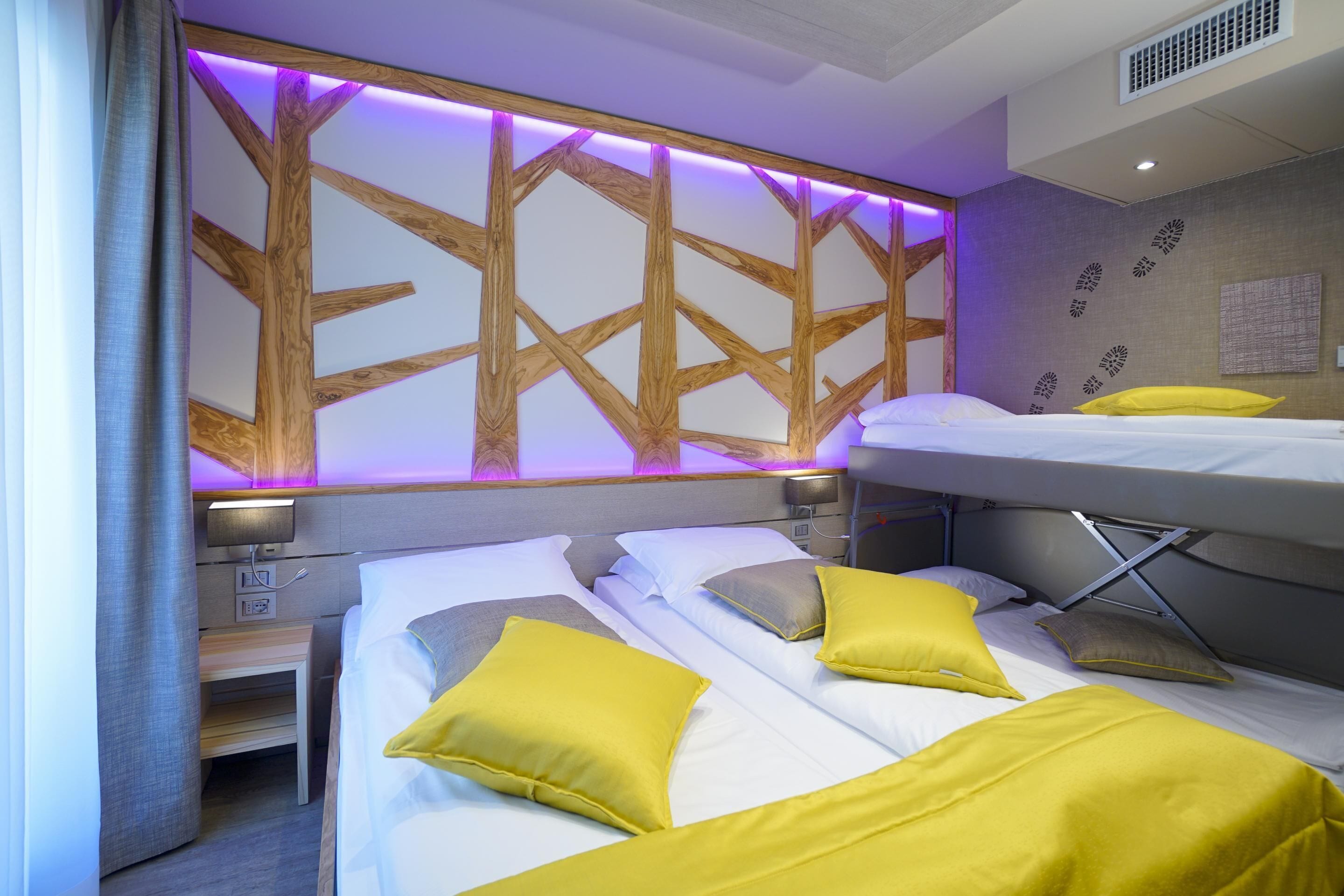 A hotel room with a bunk bed, a bedside table, and a headboard with a geometric pattern.