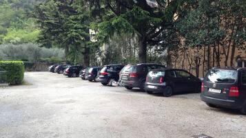 Un estacionamiento con varios coches aparcados en fila, rodeado de árboles y un edificio al fondo.