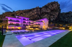 Un hotel moderno con zona de piscina, mobiliario exterior y montañas al fondo.