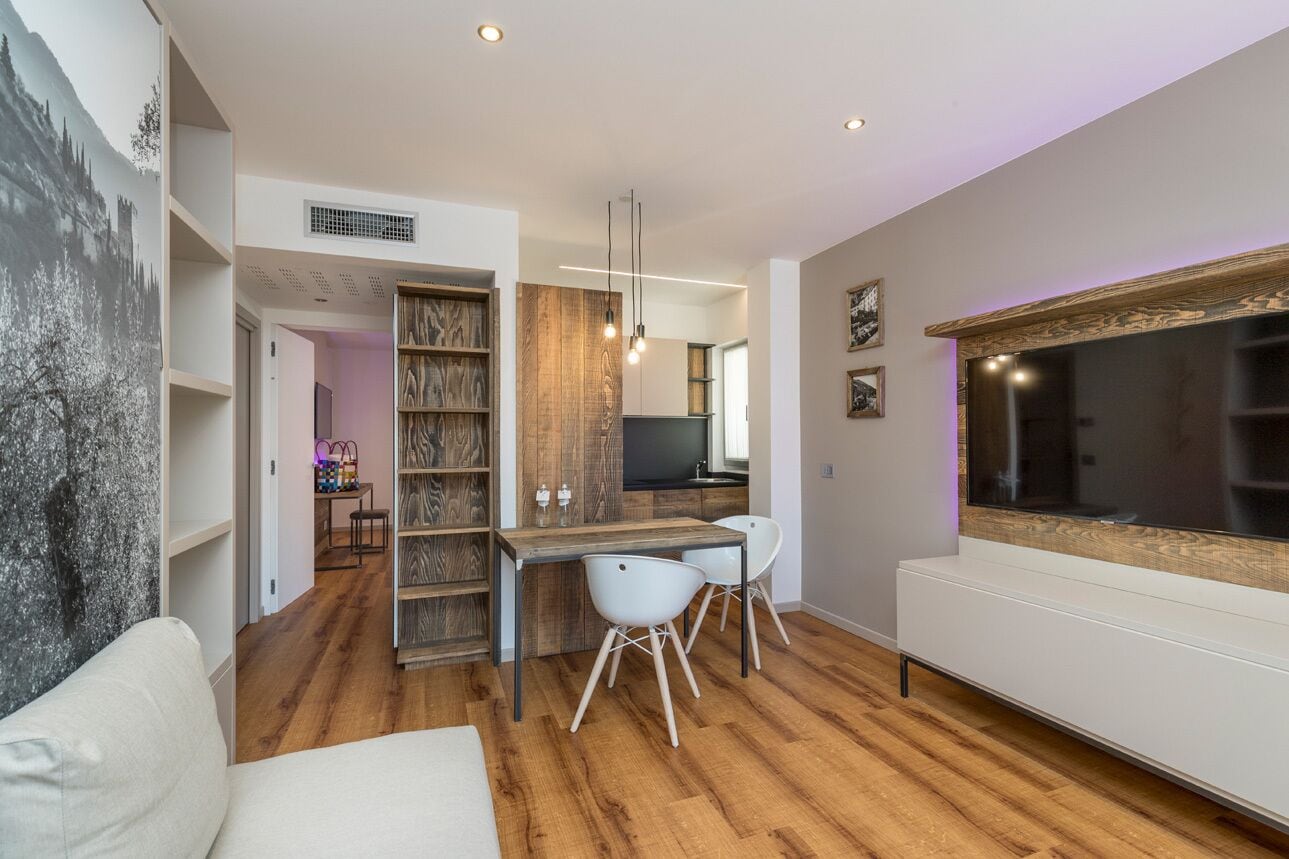 Um espaço de estar moderno com uma mesa de jantar de madeira, cadeiras brancas, um sofá e uma televisão grande.