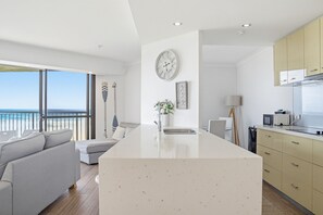 A modern kitchen with a central island, a dining area with a view of the sea, and a living room with a sofa and a large window. - The Breakers (Surfers Paradise)