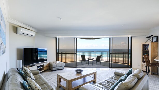 A modern living room with a large TV, comfortable seating, a coffee table, and a balcony with a view of the sea. - The Breakers (Surfers Paradise)