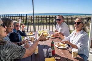 Un grupo de personas cenando en una mesa al aire libre con vistas al océano.