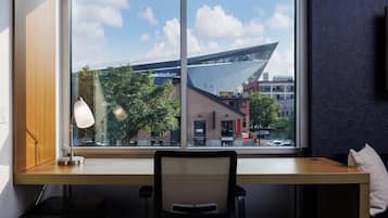A modern office space with a desk, chair, and lamp. A large window offers a view of a building with a distinctive roof and a bridge in the background.