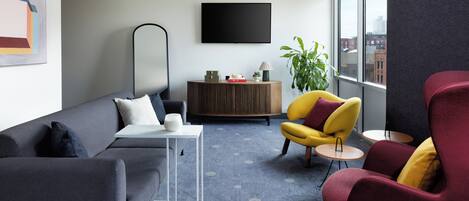 A modern living room with a grey sofa, a yellow armchair, a small table, and a large window with a view of buildings.
