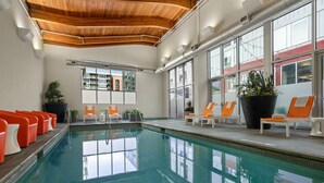 An indoor swimming pool with orange and white lounge chairs, large windows, and a wooden ceiling. - Aloft by Marriott Minneapolis (Minneapolis)