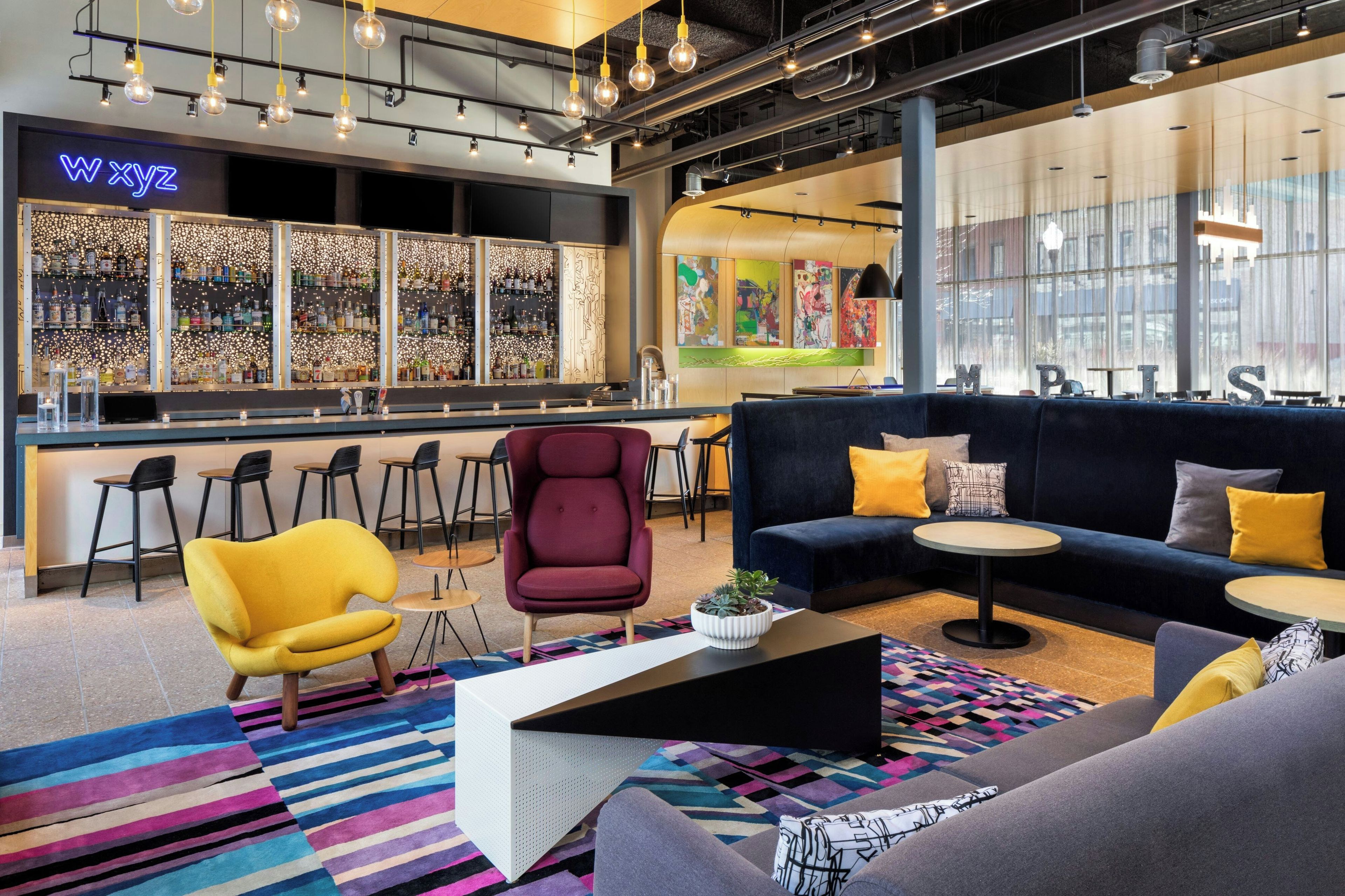 A modern bar area with a neon sign, a seating area with sofas and tables, and a colorful rug.