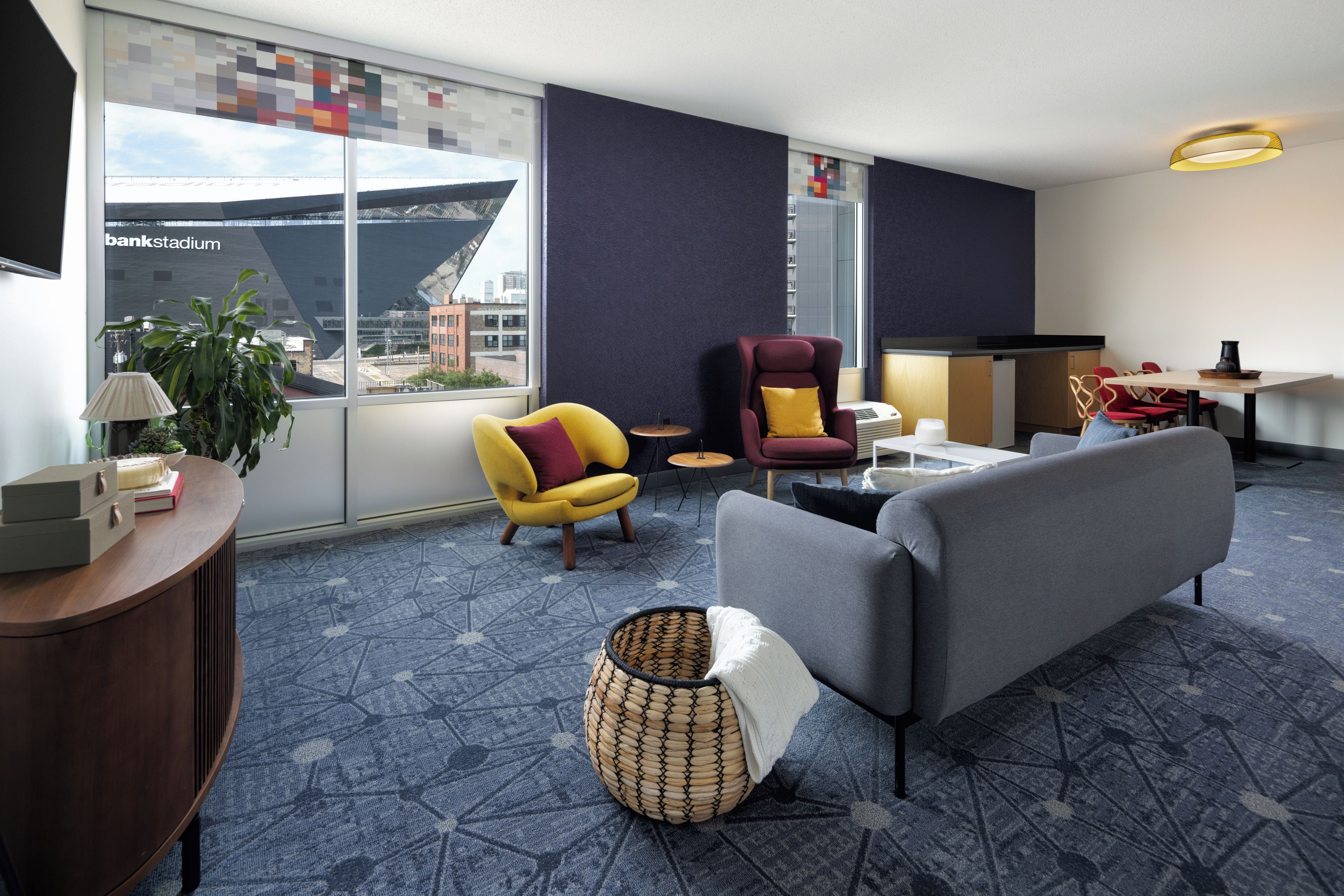 A modern hotel room with a sofa, armchairs, a small table, and a view of a stadium.