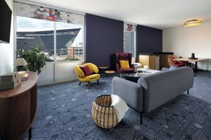 A modern hotel room with a sofa, armchairs, a small table, and a view of a stadium. - Aloft by Marriott Minneapolis (Minneapolis)