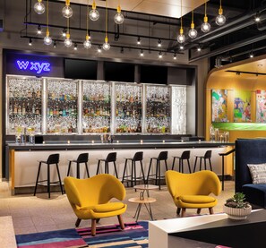 A bar area with a neon sign, a bar counter with stools, and a seating area with yellow chairs. - Aloft by Marriott Minneapolis (Minneapolis)