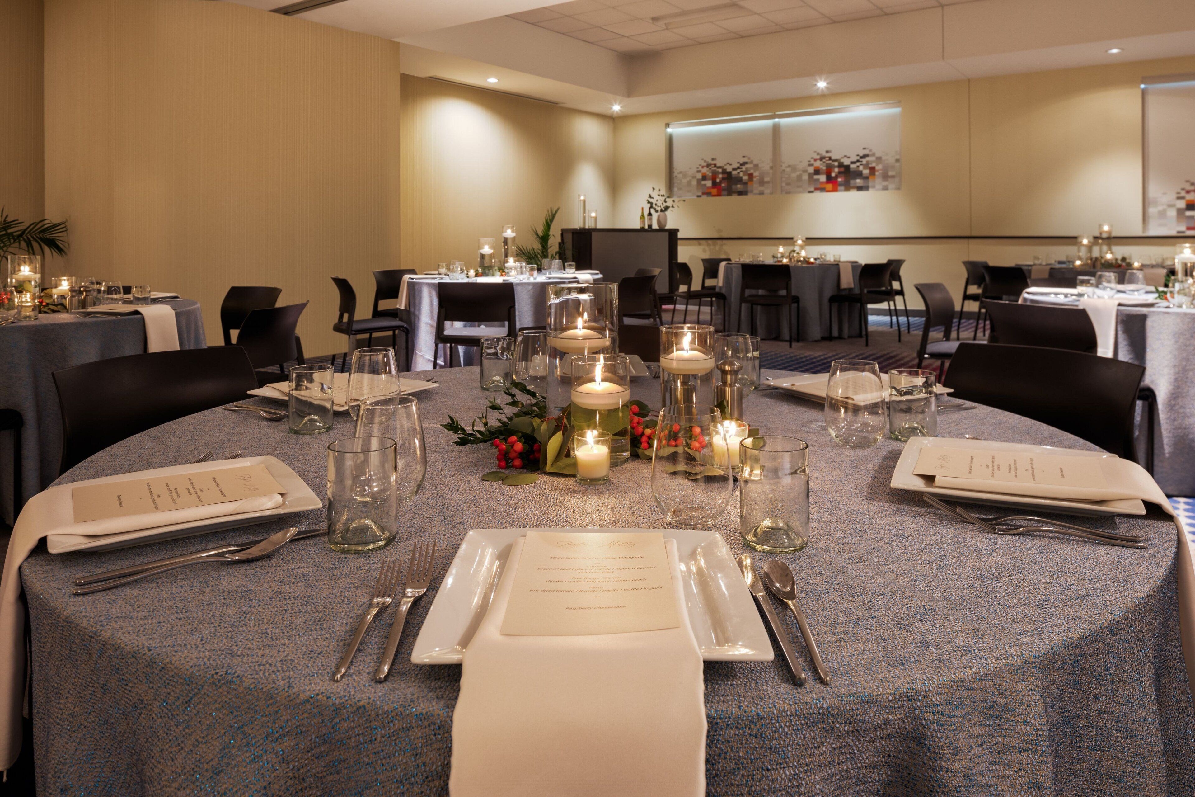 Un salón de conferencias con mesas redondas dispuestas para una comida, equipado con velas, copas y menús.