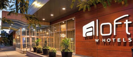Fachada moderna de un hotel, con grandes ventanales y plantas en macetas.