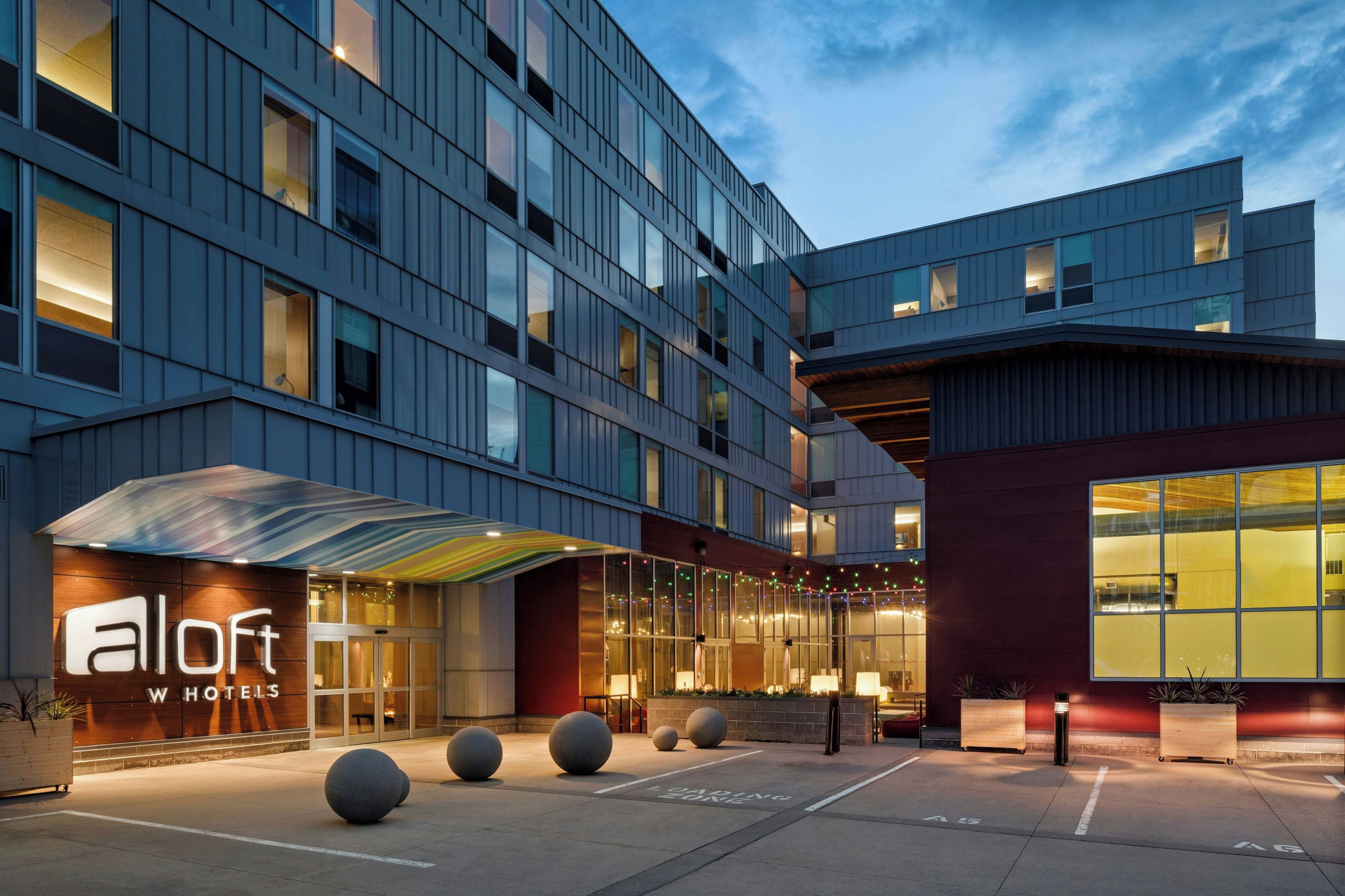 A hotel with a modern facade, a covered entrance, and a parking area.