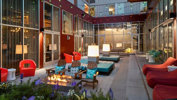 An outdoor patio area with seating, a fire feature, and a view of the building's interior. - Aloft by Marriott Minneapolis (Minneapolis)