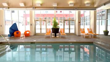 An indoor swimming pool with lounge chairs, a potted plant, and a view of a building outside.