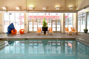 An indoor swimming pool with lounge chairs, a potted plant, and a view of a building outside. - Aloft by Marriott Minneapolis (Minneapolis)