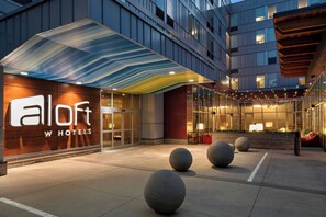 A hotel entrance with a modern facade, a glass door entrance, and a covered outdoor seating area. - Aloft by Marriott Minneapolis (Minneapolis)