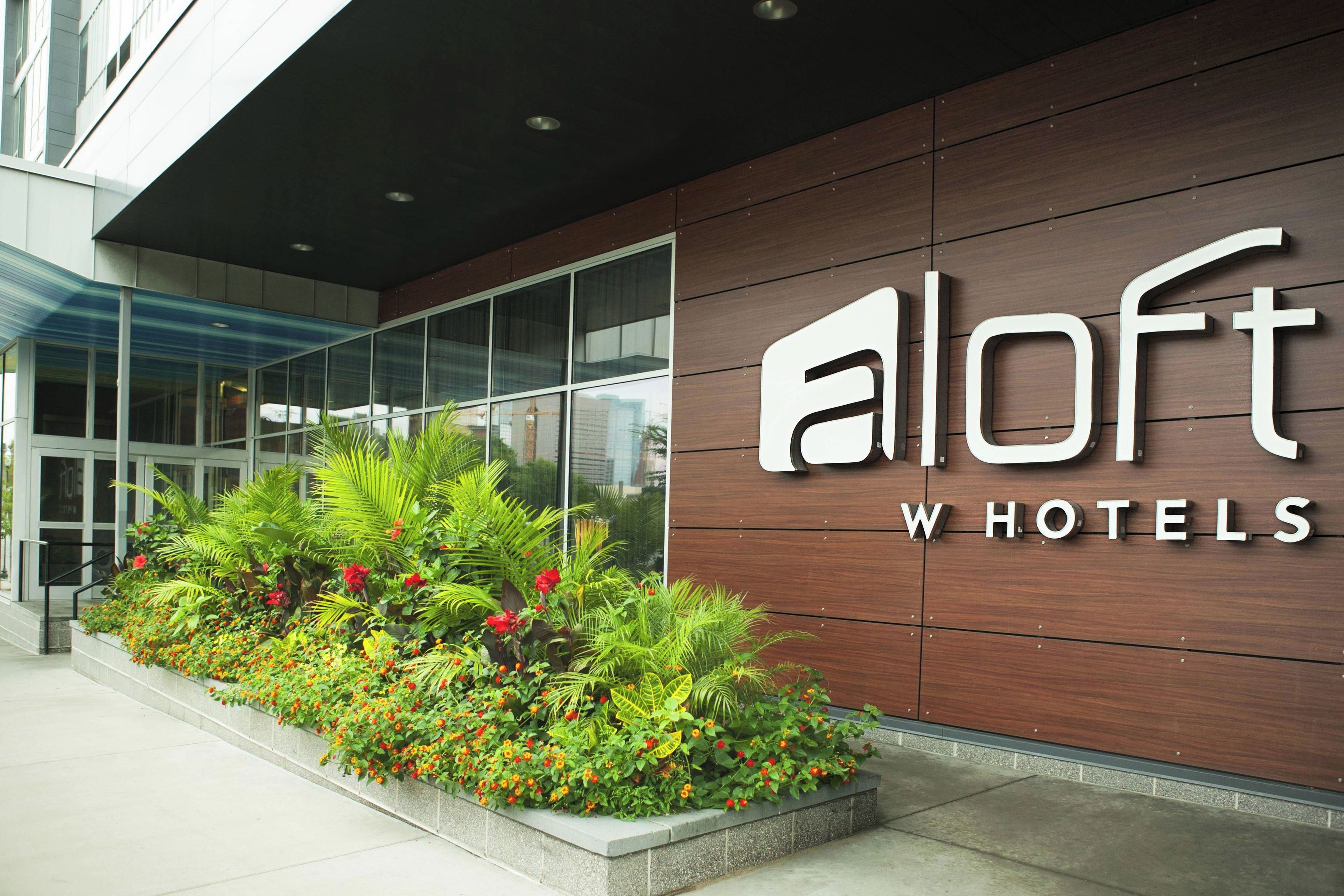 A modern building with a sign for 'aLoft WHOTELS' and a landscaped garden area with various plants and flowers.