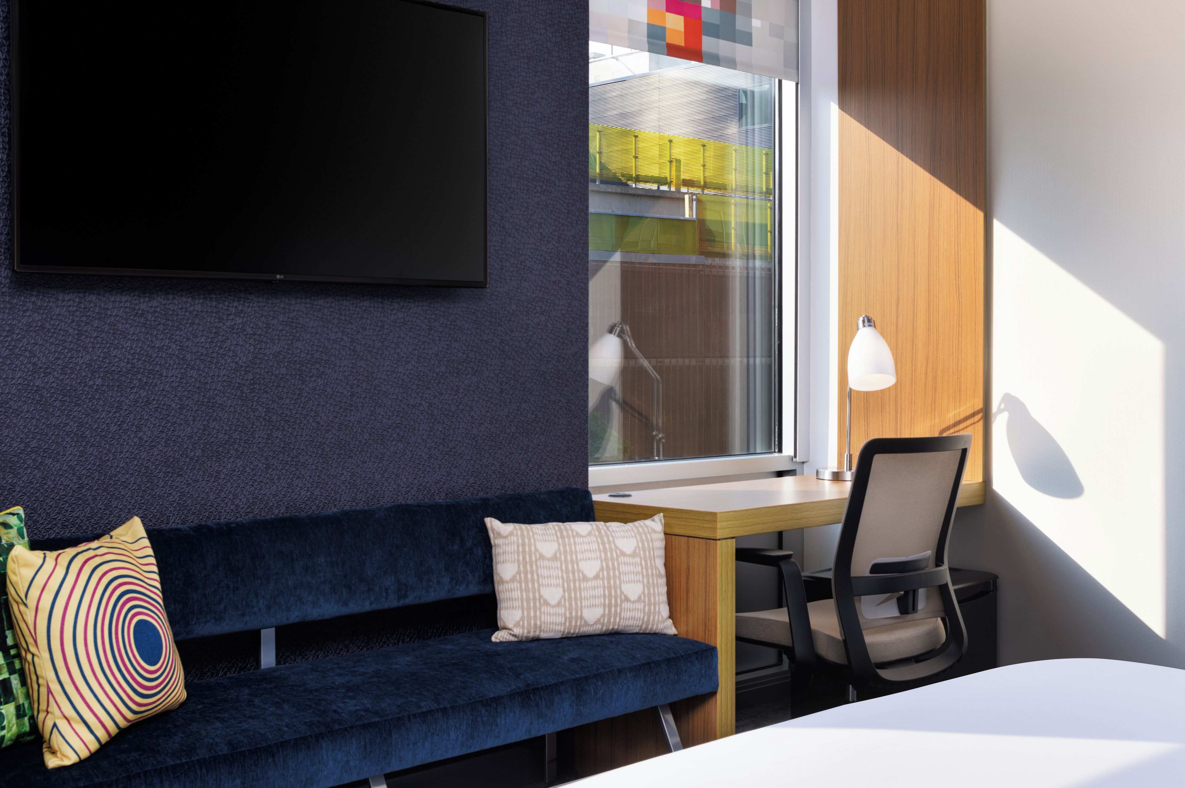 A modern room with a dark blue sofa, a wooden desk, a chair, and a TV mounted on the wall.