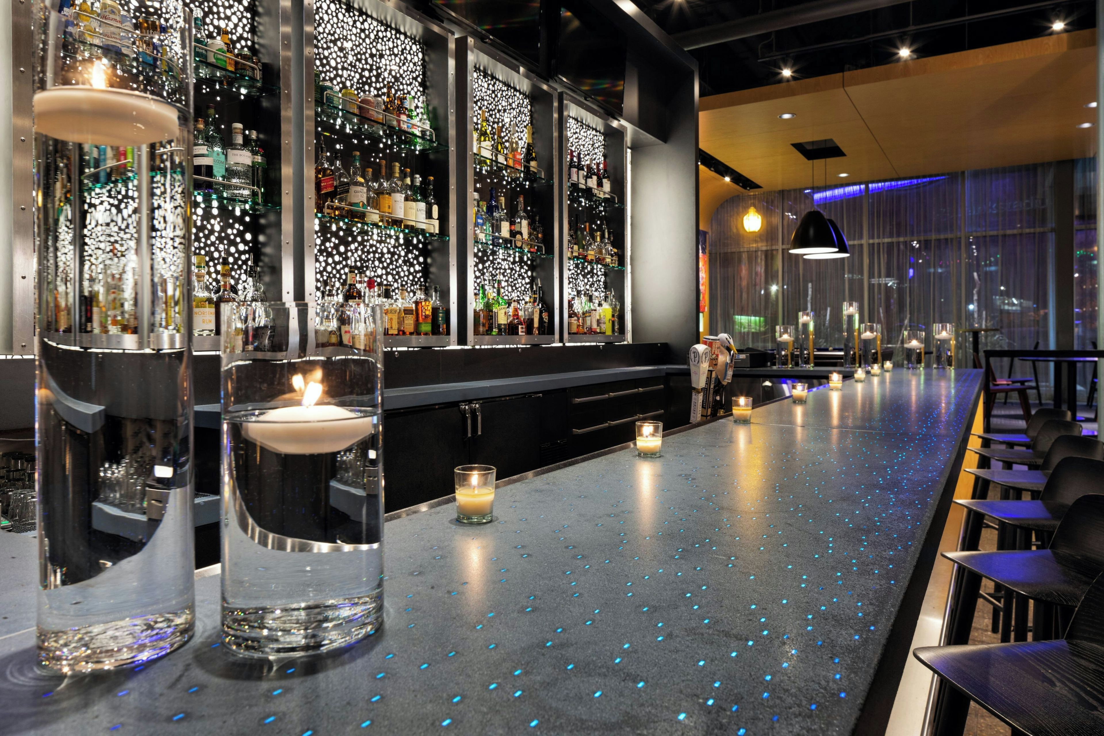 Una zona de bar con una barra larga, varias botellas de alcohol y velas.