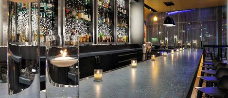 Una zona de bar con una barra larga, varias botellas de alcohol y velas.