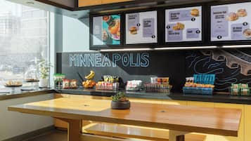 A modern restaurant interior with wooden tables, hanging pendant lights, and a menu board displaying food items.