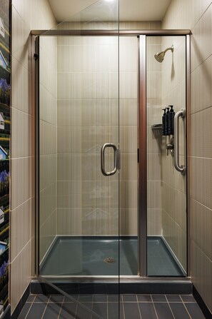 A glass-enclosed shower stall with a handrail, a showerhead, and a bottle of shampoo. - Aloft by Marriott Minneapolis (Minneapolis)
