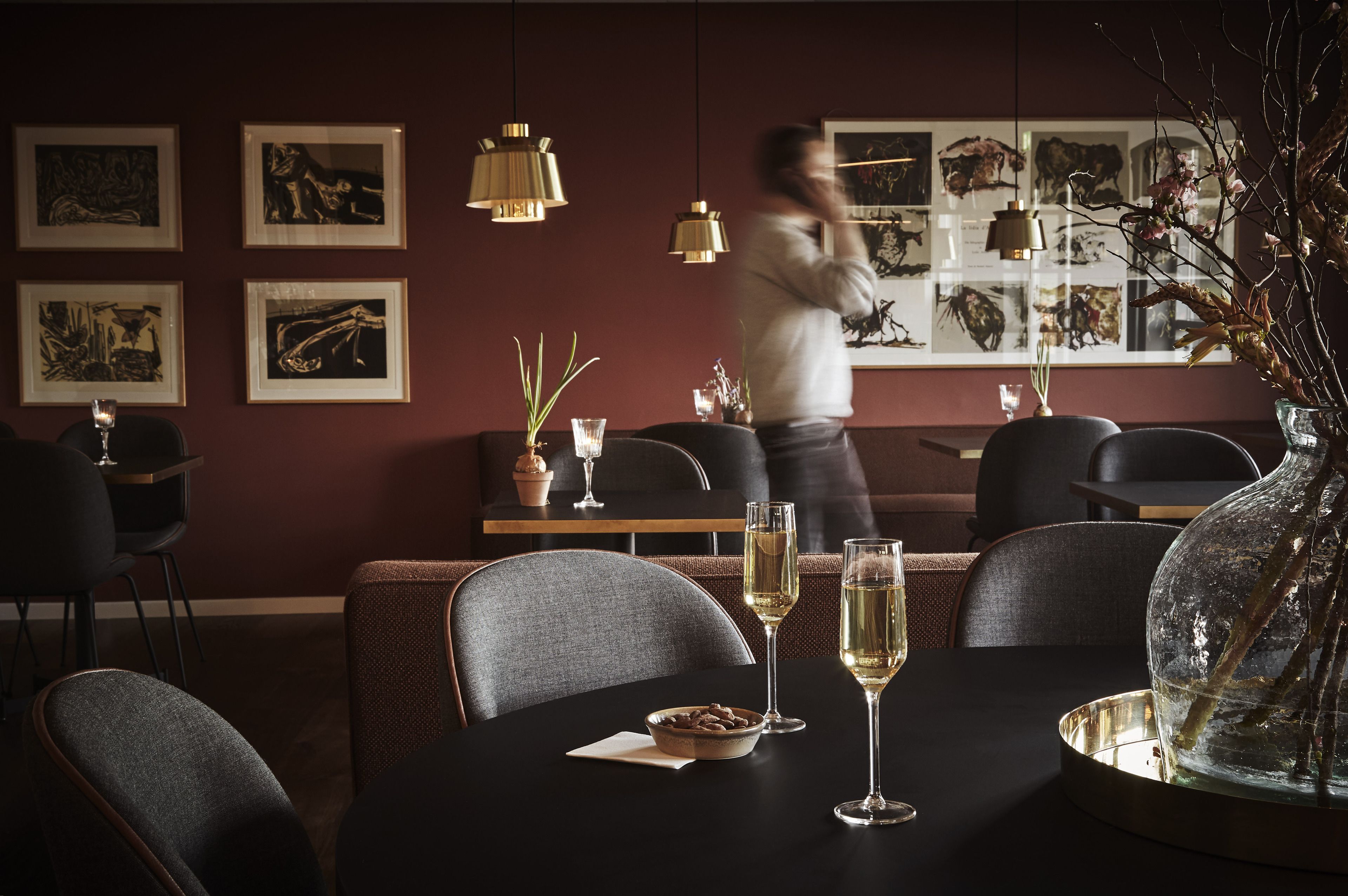 En restaurant med mørkt interiør, billeder i rammer på væggene og en tjener i bevægelse.