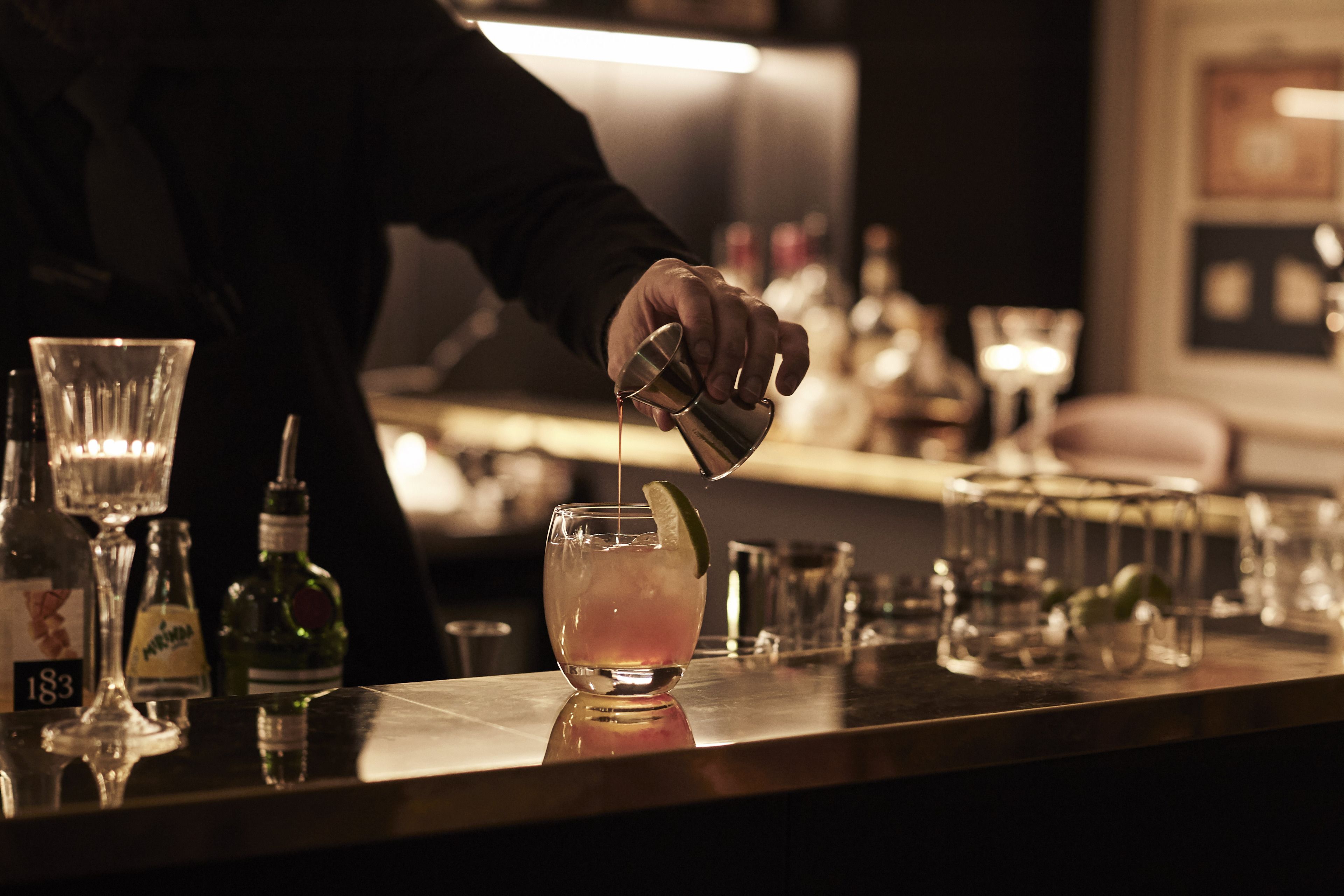 A bartender pouring a drink into a glass with a lime wedge.
