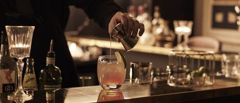 A bartender pouring a drink into a glass with a lime wedge.