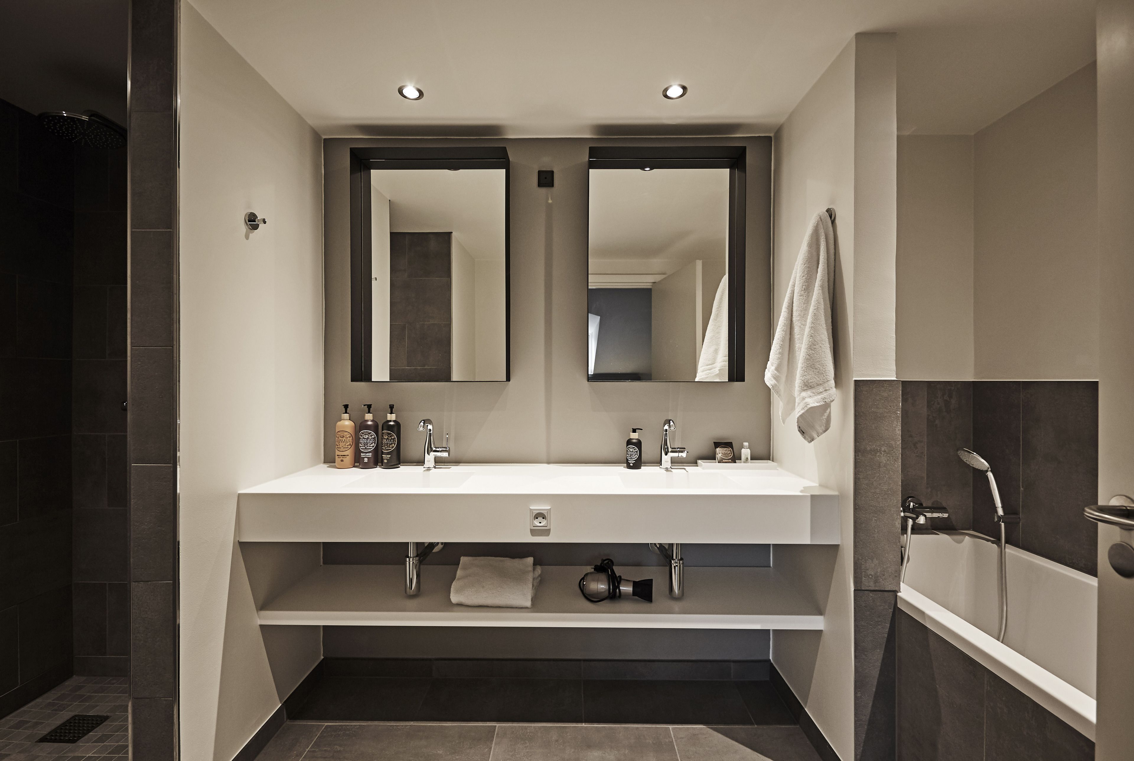 A modern bathroom with a double sink, two mirrors, a vanity, and a bathtub.
